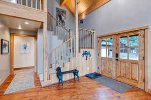 Un intérieur spacieux avec un escalier en bois, une grande porte en bois dotée de panneaux de verre et une vue sur l’extérieur.