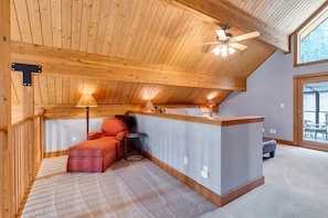 A cozy attic bedroom with a wooden ceiling, a ceiling fan, a small desk, and a comfortable chair. - Cozy Mountain Cabin Close to Town (Darby)