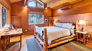 Ein gemütliches Schlafzimmer mit einem Holzbett, zwei Nachttischen, einem Fenster mit Blick ins Freie und einer Decke mit sichtbaren Balken.