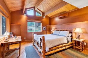 Un dormitorio acogedor con una cama de madera, dos mesitas de noche, un ventanal con vistas al exterior y un techo con vigas a la vista.