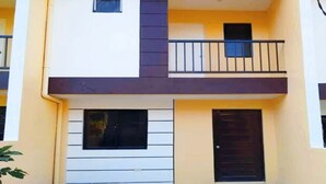 Un edificio di due piani con un balcone al piano superiore, un'entrata principale e una piccola finestra.