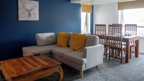 A living room with a grey sofa, wooden coffee table, and a dining table with chairs. - Modern Unit Cook  Work in Comfort (Motherwell)