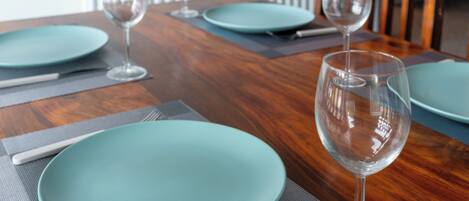A dining table with teal plates, clear wine glasses, and a wooden table surface.