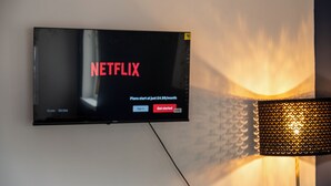 A flat-screen TV mounted on a wall displaying the Netflix logo and sign-up options. - Modern Unit Cook  Work in Comfort (Motherwell)