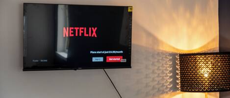 A flat-screen TV mounted on a wall displaying the Netflix logo and sign-up options.