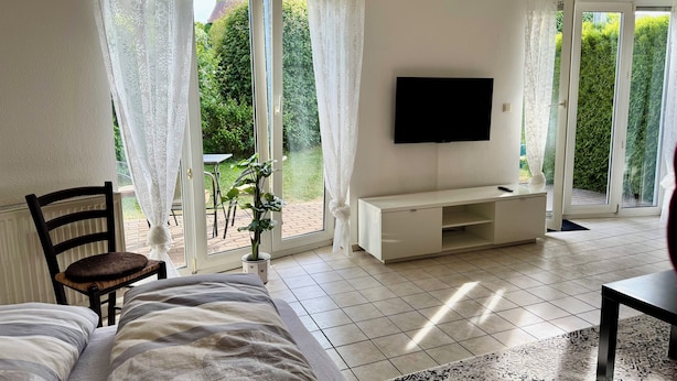 A bedroom with a bed, a TV mounted on the wall, and a sliding glass door leading to a patio. - Small idyll: Quiet & relaxing - Peter M22 (Stadtsteinach)