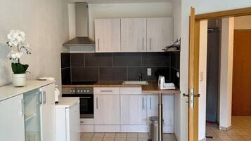 A compact kitchen with white cabinets, a small refrigerator, a stove, and a sink.