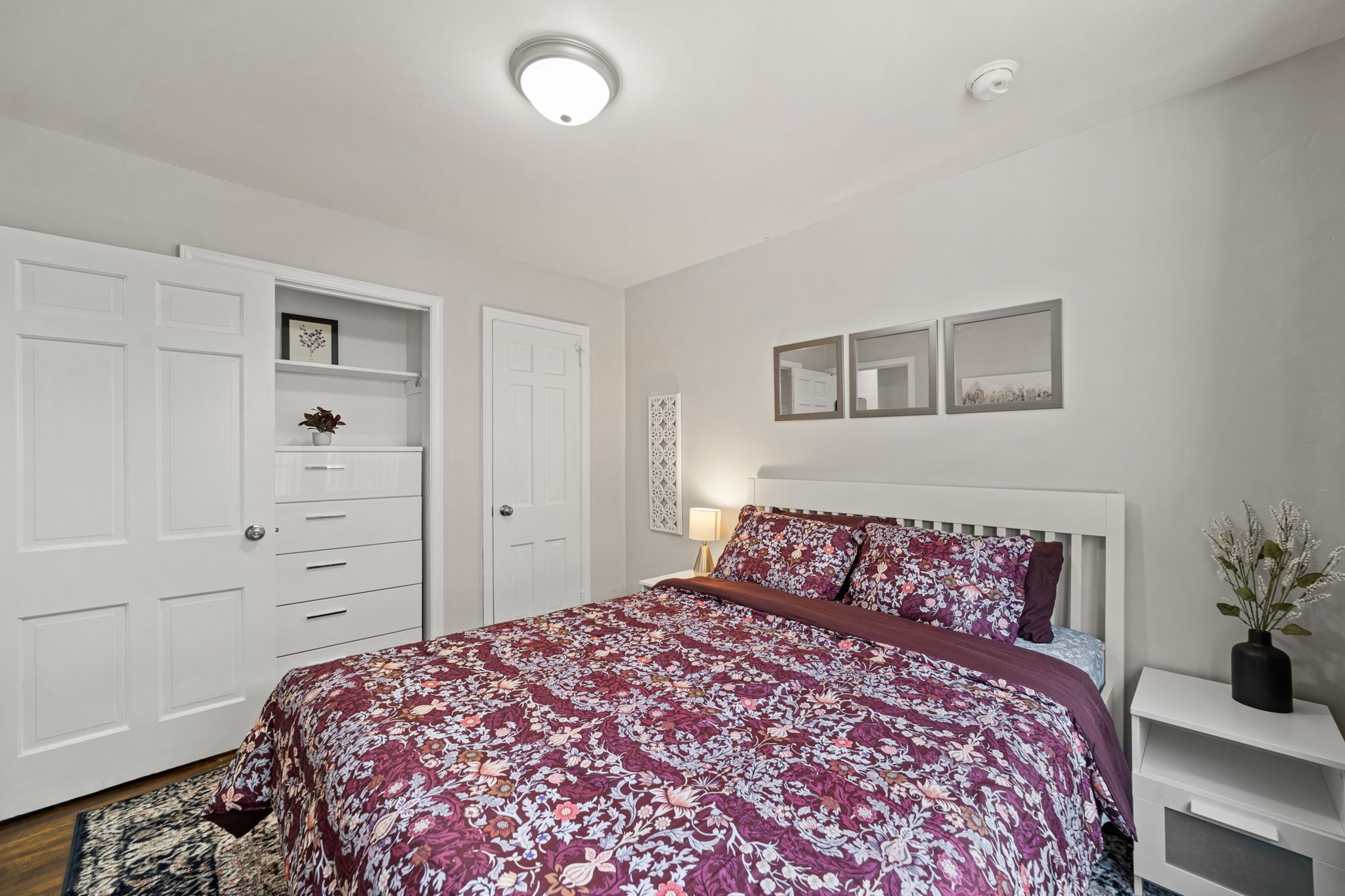 Une chambre avec un grand lit, une armoire blanche et une table de chevet sur laquelle se trouve un vase.
