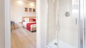 A modern hotel room with a glass shower enclosure, a bed with a red and white bedspread, and a small seating area with a chair. - Elegance and Relaxation in the center of Cagliari - King Standard (Cagliari)