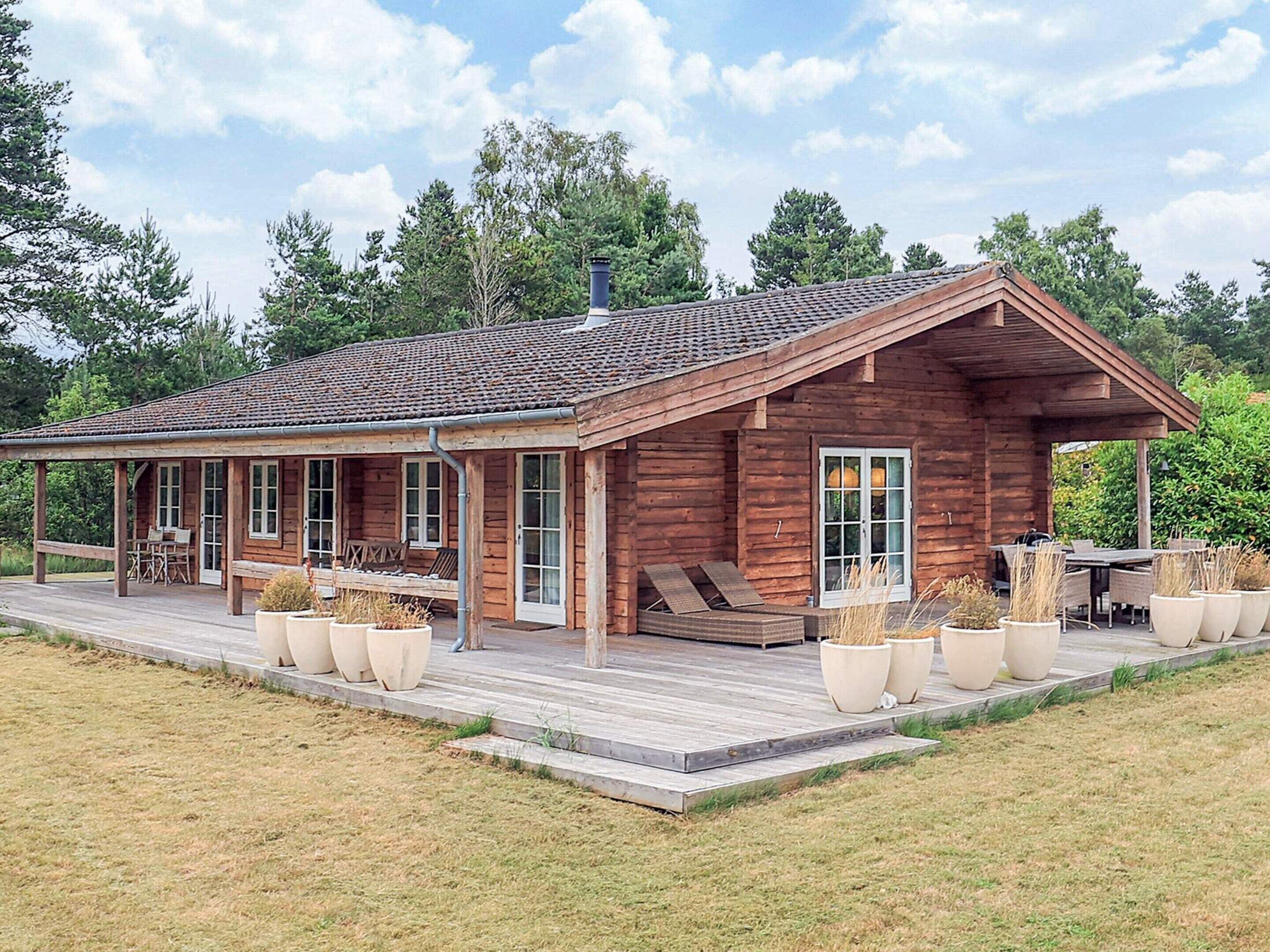Eine Holzhütte mit verdeckter Veranda, Sitzgelegenheiten im Freien und großen Pflanzkübeln.