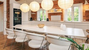 Una cocina moderna con una isla grande, taburetes blancos para bar y luces colgantes.