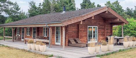 A wooden cabin with a covered porch, outdoor seating, and potted plants.