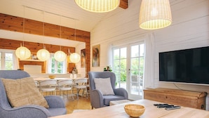 Una sala de estar moderna con un televisor grande, sofás grises, una mesa de centro de madera y una zona de comedor con sillas blancas.