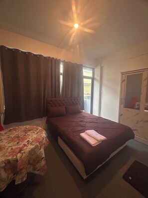 A bedroom with a large bed, a smaller bed, a window with curtains, and a wardrobe.