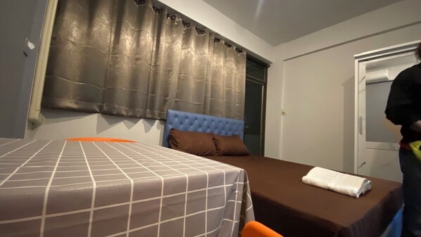 A hotel room with a single bed, a blue headboard, and a window with curtains.