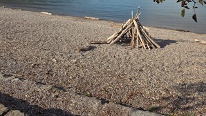 Una playa de guijarros con un montón de troncos, un lago tranquilo y una cadena montañosa distante.