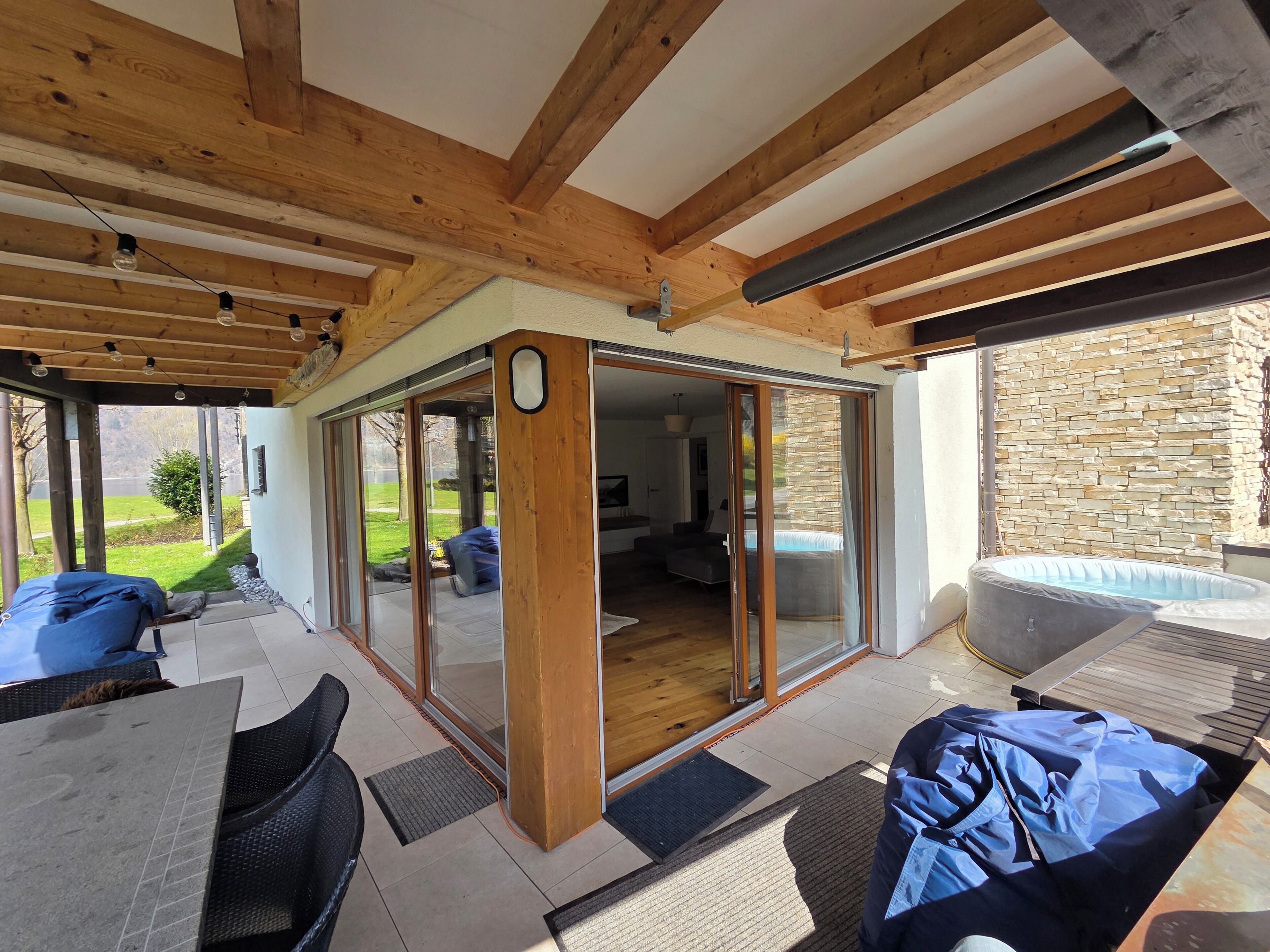 Een overdekt terras met een schuifdeur naar een woonkamer, tuinmeubels en een jacuzzi.