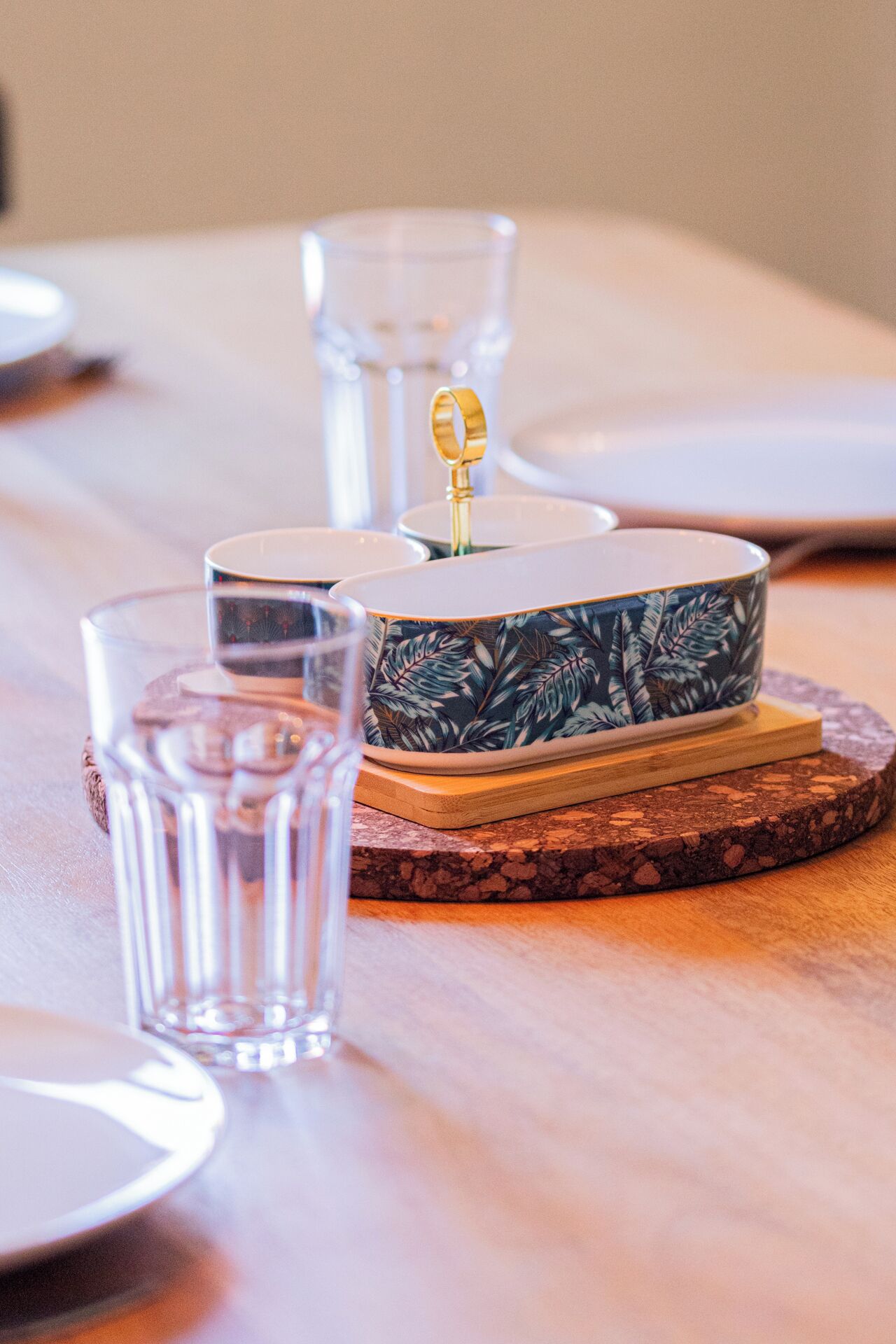 Une table avec un bol décoratif posé sur un dessous de verre, un verre d’eau et un verre transparent.