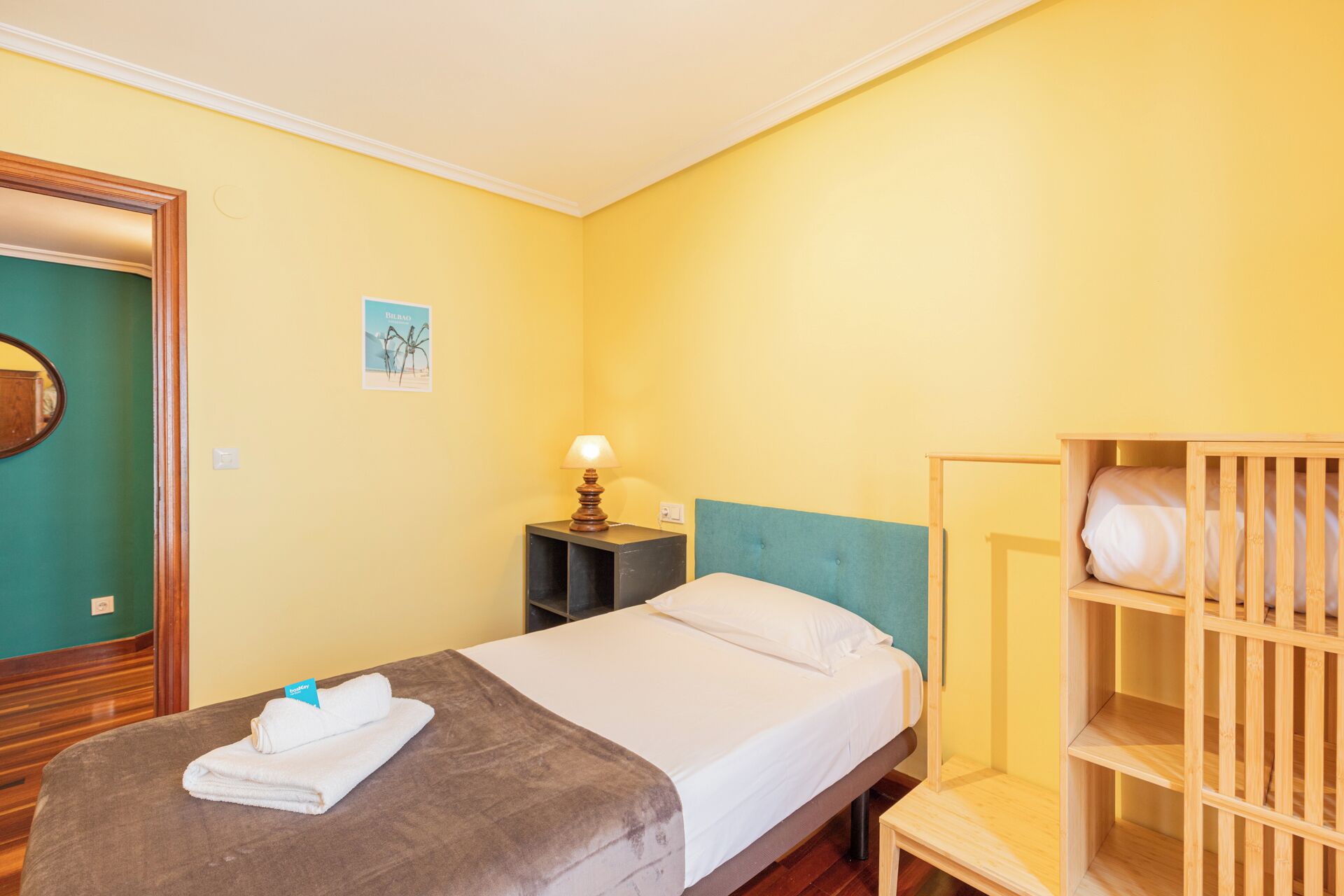 Une chambre d’hôtel avec un lit, une table de chevet, une lampe, un berceau en bois et une porte.
