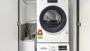 A compact laundry room with two stacked front-loading washing machines, a small cabinet with detergent bottles, and a sink. - Modern 2-Bedroom Apartment in Melbourne CBD with Balcony, Pool & Gym Access (Melbourne)
