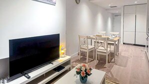 A modern living room with a flat-screen TV, a dining area with a table and chairs, and a large wardrobe in the background. - Modern 2-Bedroom Apartment in Melbourne CBD with Balcony, Pool & Gym Access (Melbourne)