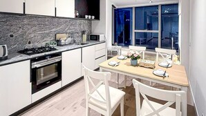 A modern kitchen with white cabinets, a built-in oven, and a dining area with a wooden table and white chairs. - Modern 2-Bedroom Apartment in Melbourne CBD with Balcony, Pool & Gym Access (Melbourne)