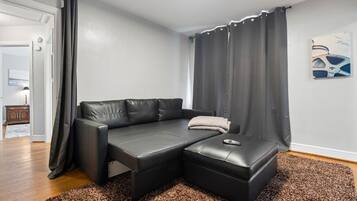 A modern living room with a black leather sofa, a matching ottoman, and a brown speckled rug.