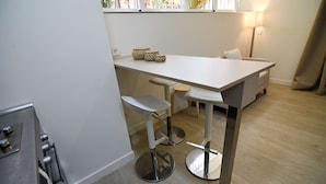 Une cuisine moderne avec un comptoir blanc, deux tabourets de bar et une petite table.