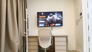 Un espace de bureau moderne comprenant un bureau, une chaise et un téléviseur fixé au mur qui diffuse un jeu vidéo.