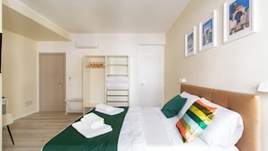Une chambre d’hôtel avec un lit, une couvre-lit verte, du linge de lit blanc, une tête de lit marron et un mur orné de tableaux.