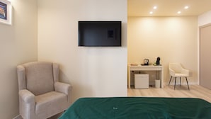 Une pièce comprenant un lit, une chaise, un bureau avec un ordinateur et un téléviseur fixé au mur.