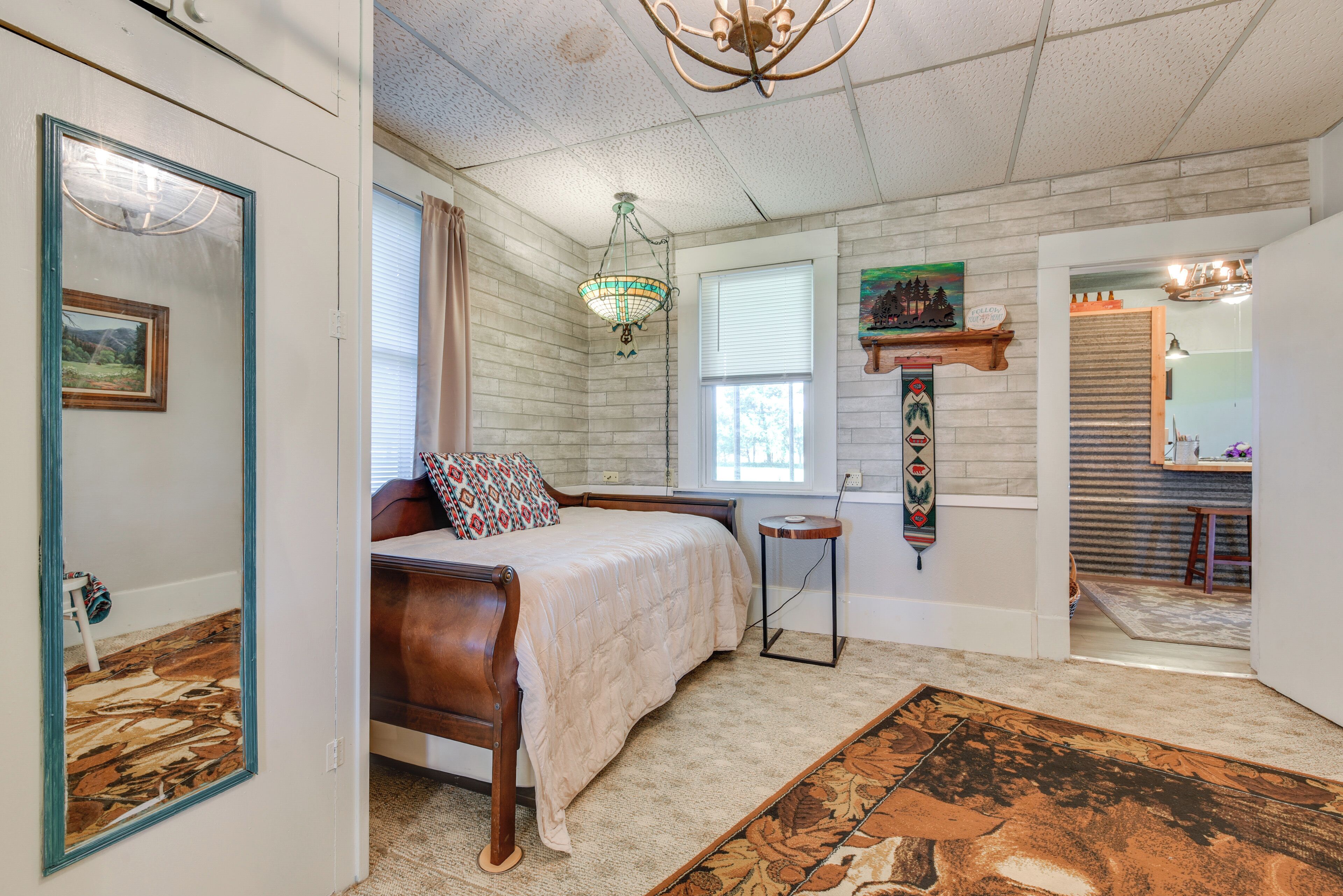 A bedroom with a bed, a hanging light fixture, a window, and a door leading to another room.