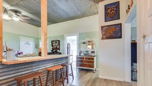 Una cocina con barra, taburetes de madera, estante para café y alfombra estampada.