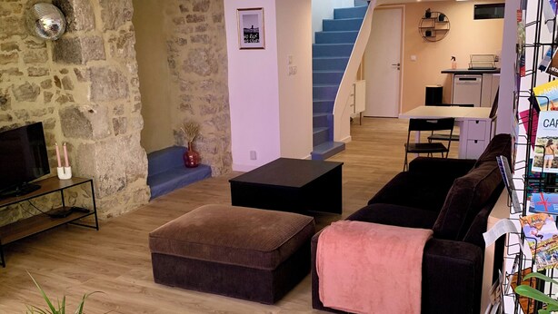 A modern living room with a stone wall, a sofa, a coffee table, and a bookshelf. - Large duplex in the heart of the village of Carnac, near historic sites & beaches (Carnac)