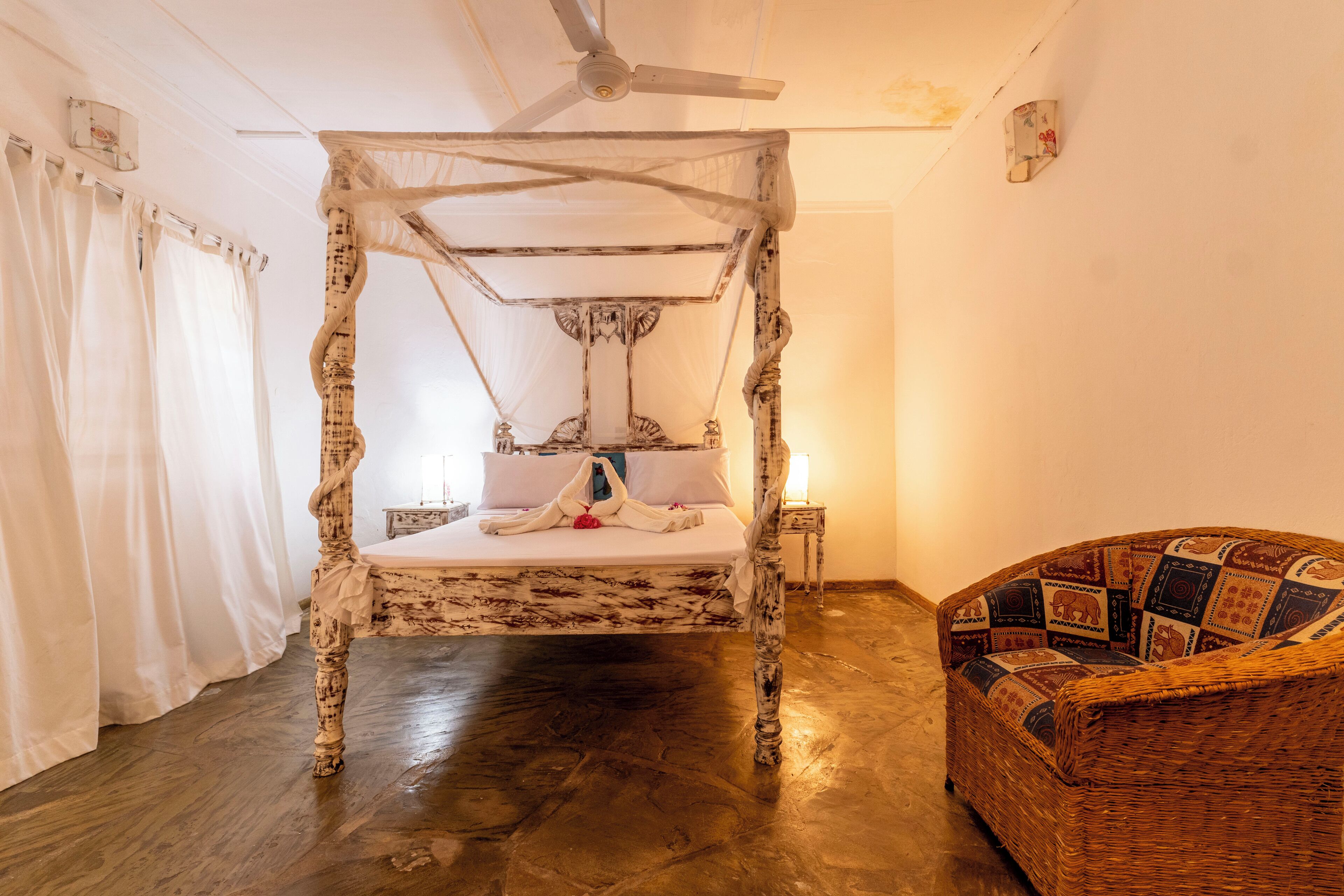 Una habitación con cama con dosel, un sillón de mimbre y un ventilador de techo.