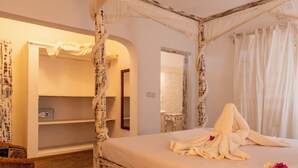 A four-poster bed with a white canopy, a bedside table, a mirror, and a shelf with a radio. - Paradise Lagoon B&B (Watamu)
