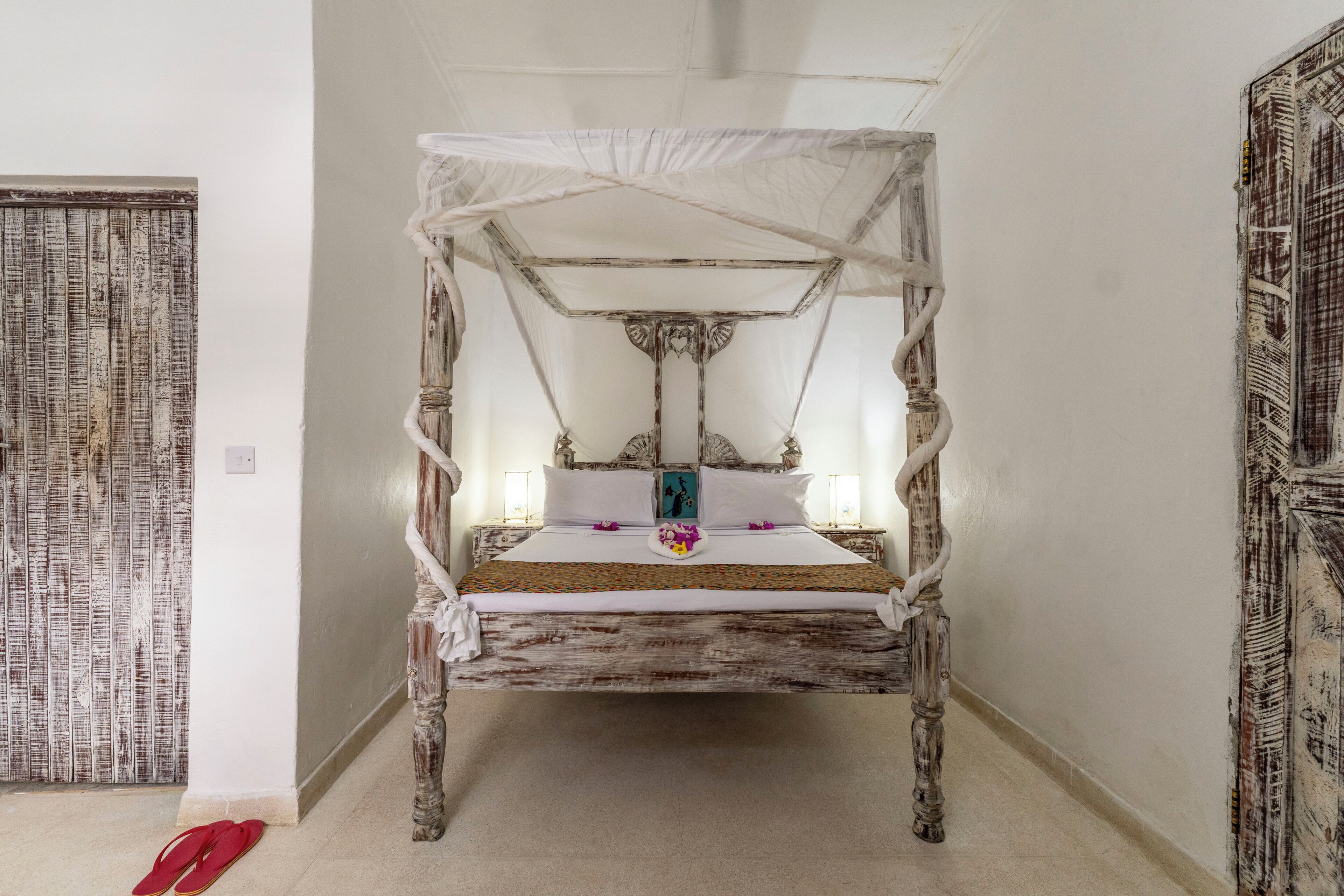 Een hemelbed met houten frame en witte beddengoed.