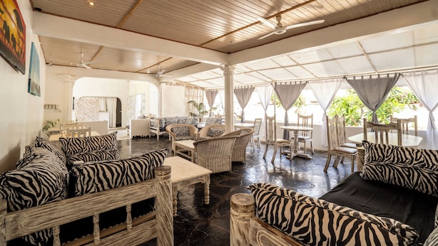 A spacious indoor area with wicker furniture, ceiling fans, and large windows allowing natural light. - Paradise Lagoon B&B (Watamu)