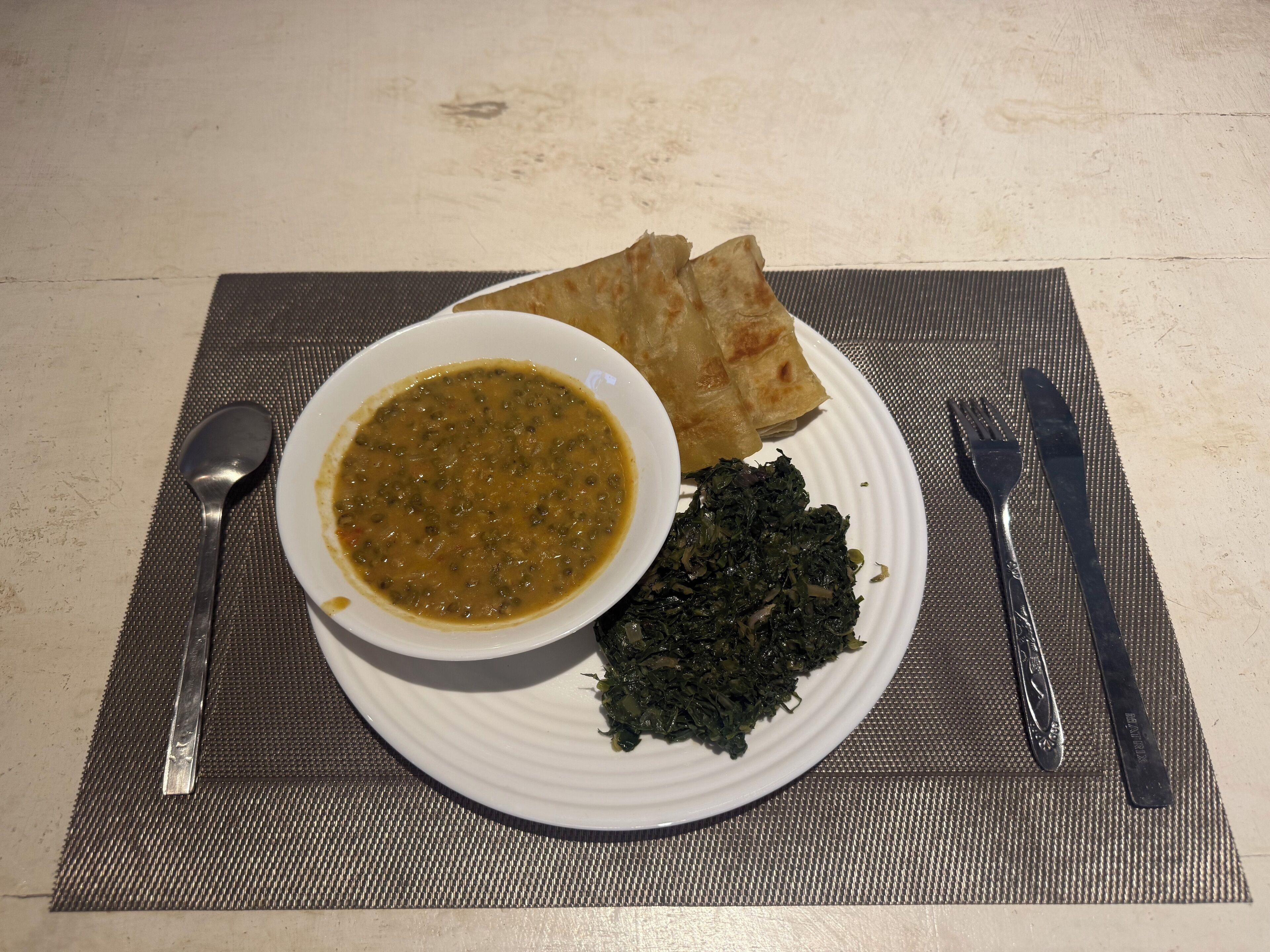 A plate with a bowl of soup, flatbread, and greens on a placemat.