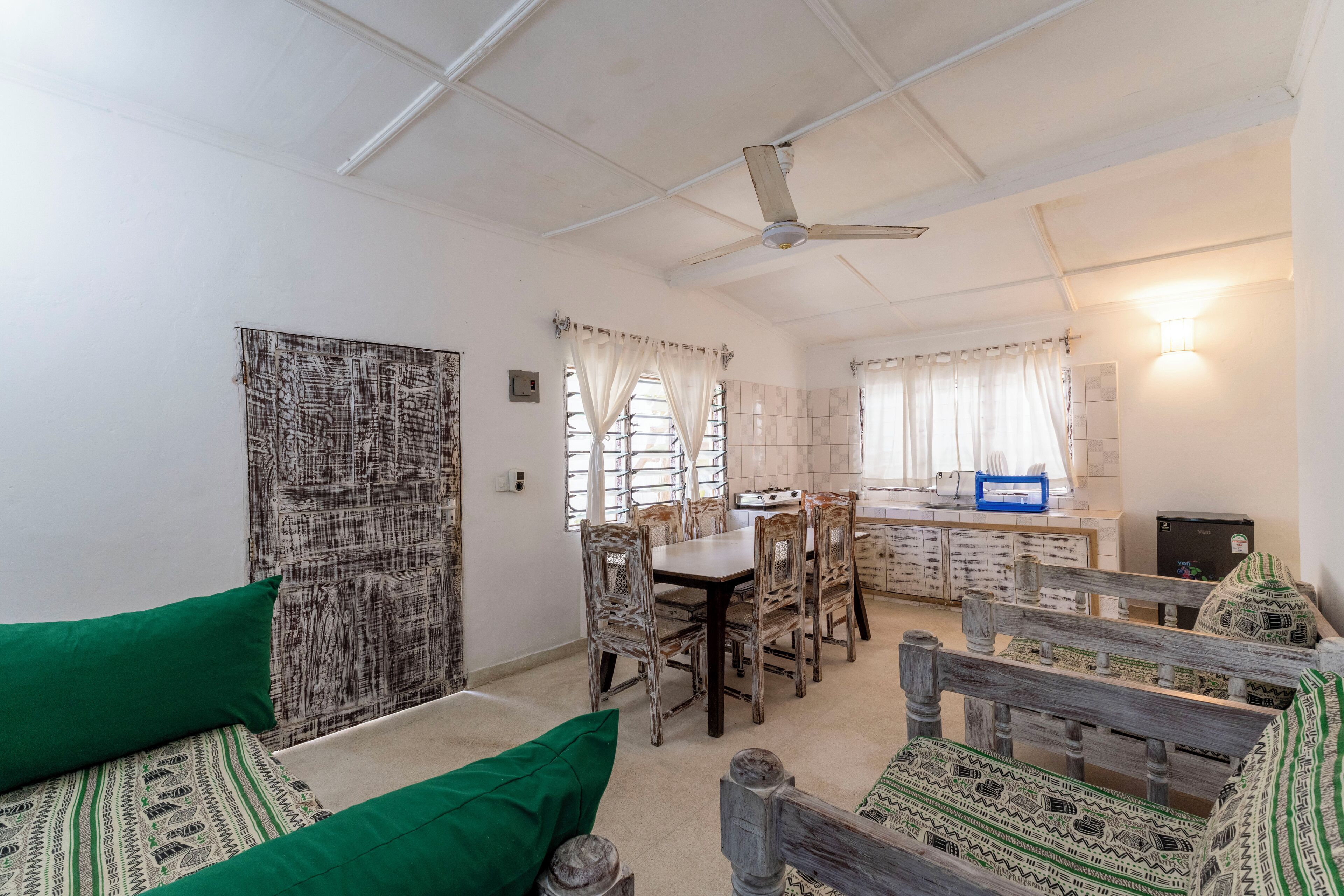 A room with a dining table, chairs, a sofa, and a ceiling fan.