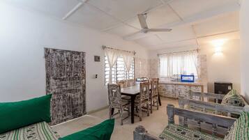 A room with a dining table, chairs, a sofa, and a ceiling fan.