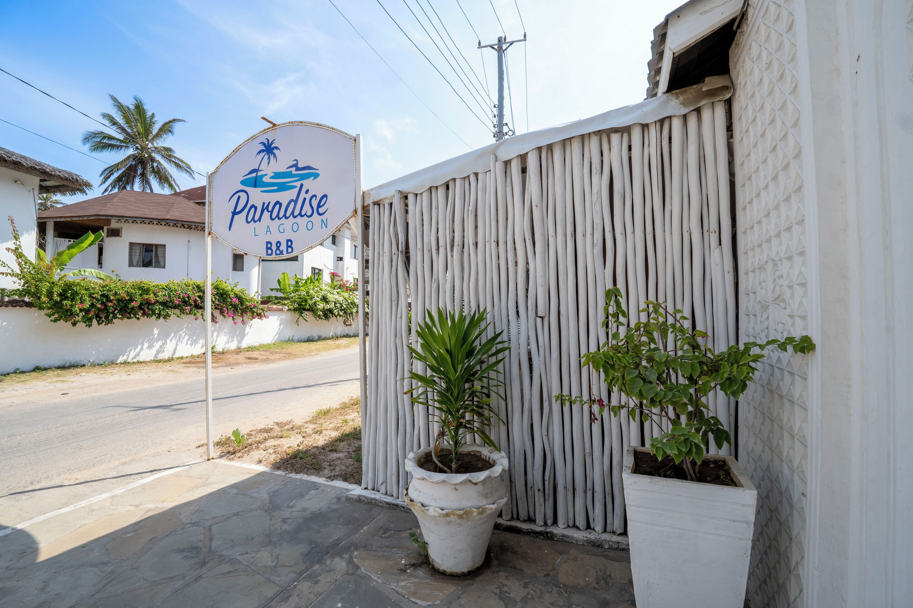 A white building with a sign reading "Paradise Lagoon B&B" and a wooden fence.