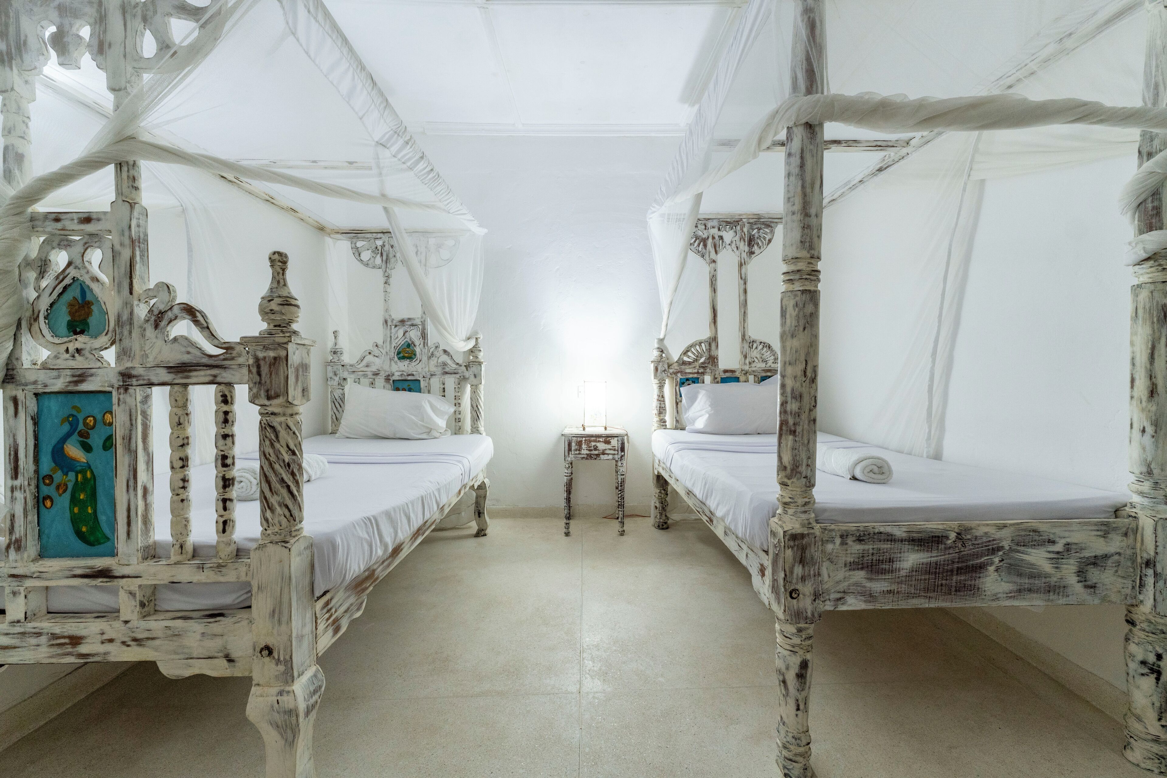 Una habitación con dos camas bajo dos doseles blancos, una mesita y un espejo decorativo.