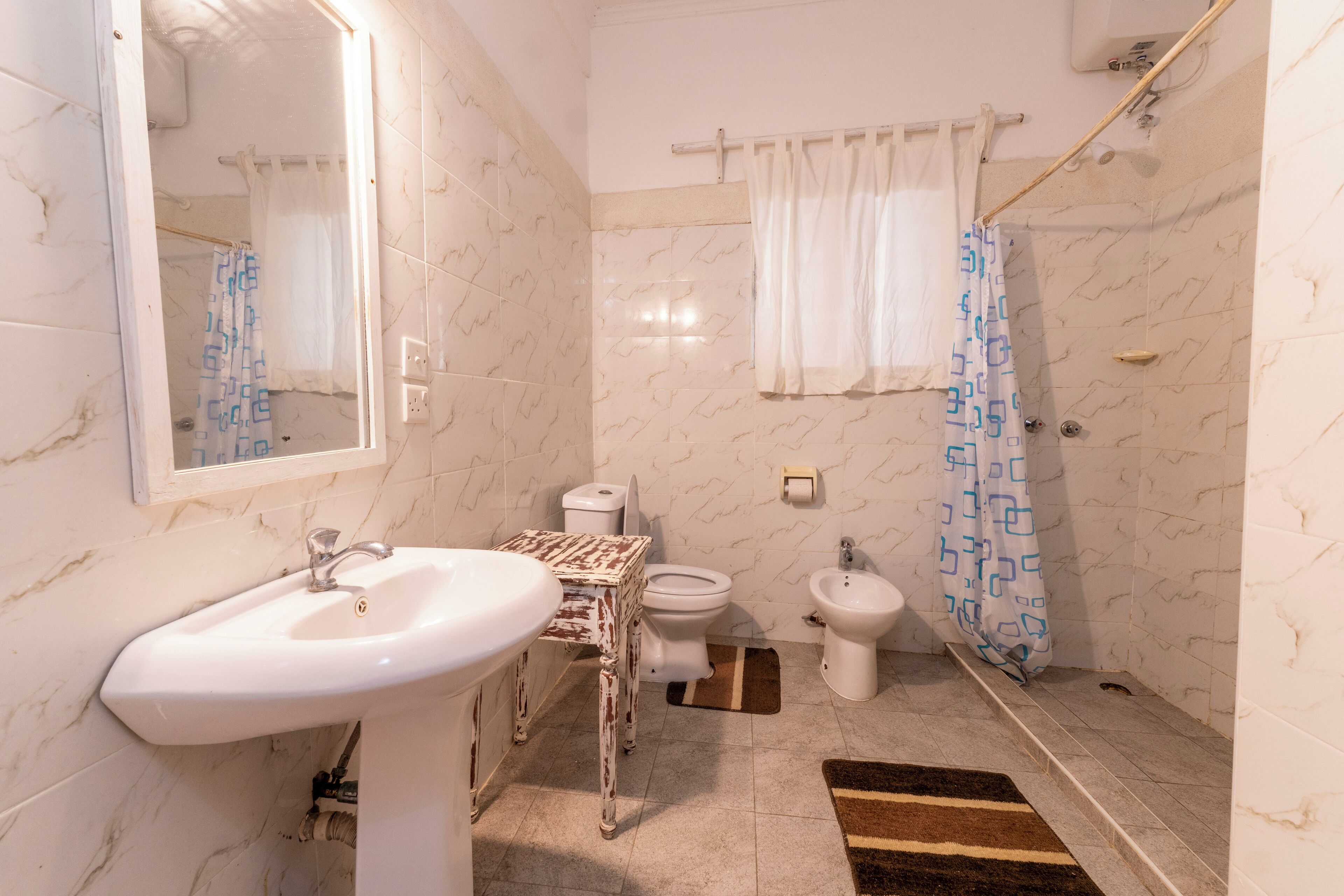 A bathroom with a sink, toilet, bidet, and shower curtain.