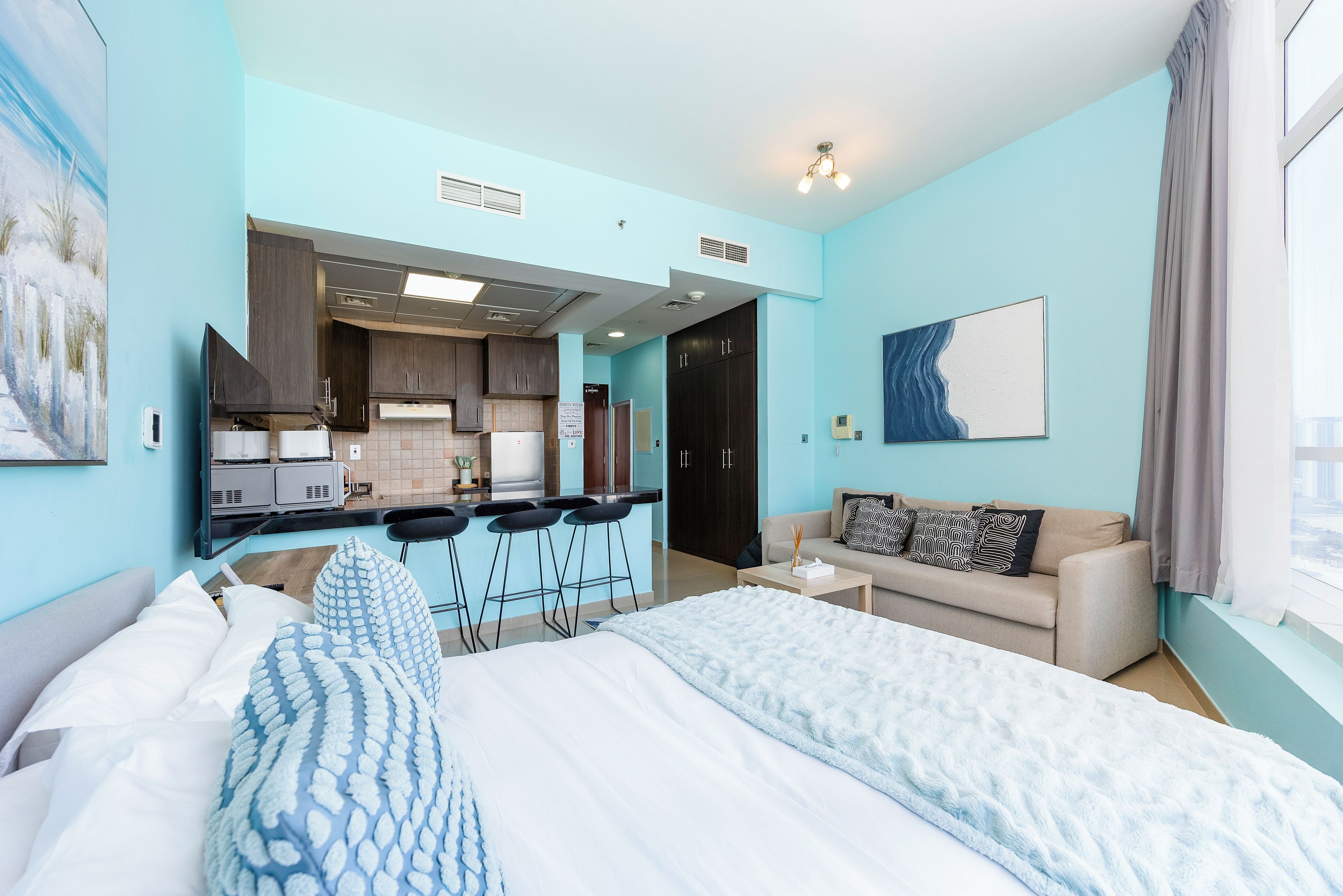 Habitación de hotel moderna con cama, sofá, kitchenette y vistas a la ciudad.