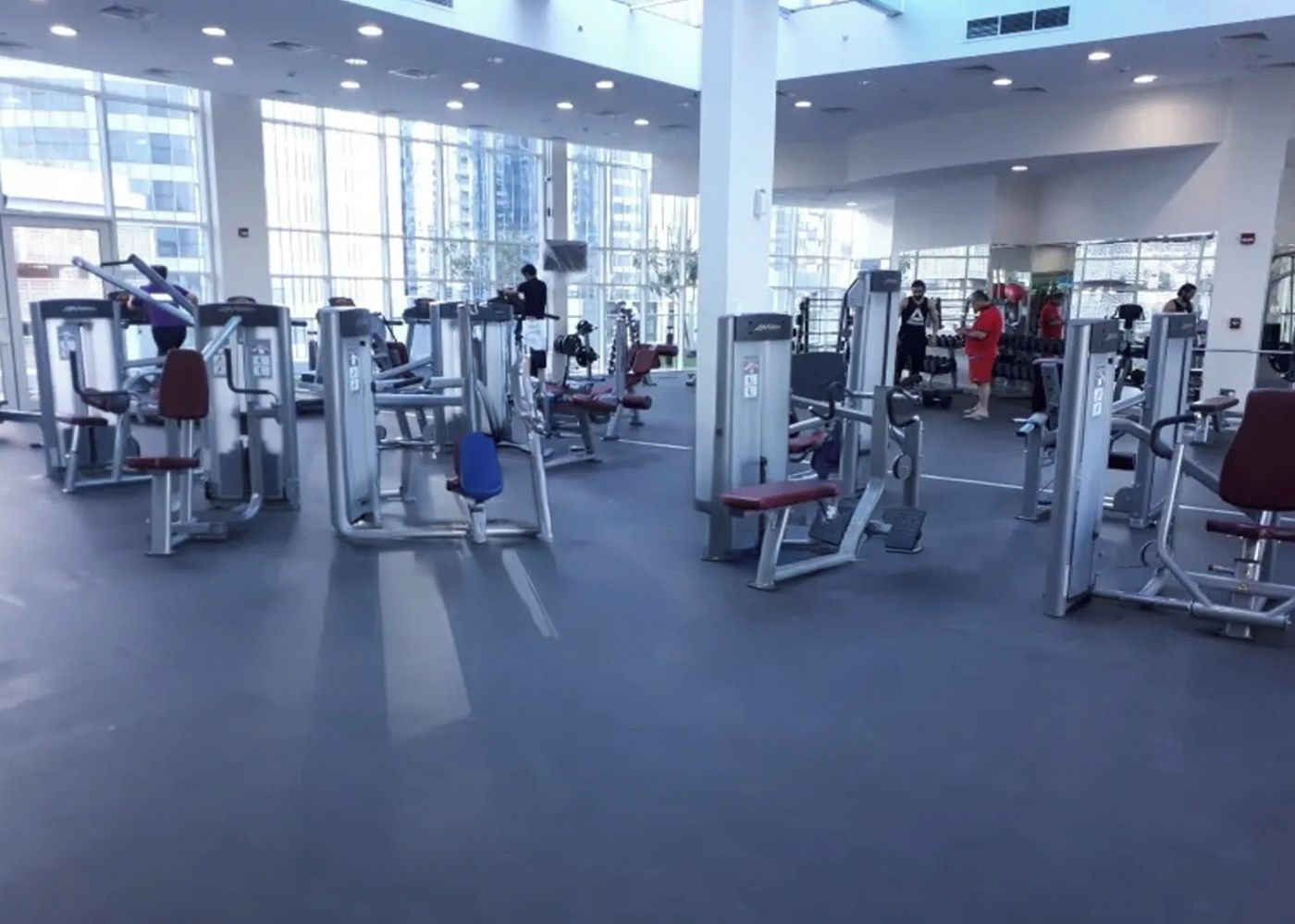 Une salle de sport équipée de divers appareils d’exercice et dotée de grandes fenêtres laissant entrer la lumière naturelle.