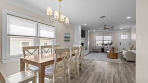 A spacious living room with a wooden dining table, white chairs, and a ceiling fan. - Buddy's Sandcastle: room for family, friends, and pets. Fenced yard. (Atlantic Beach)