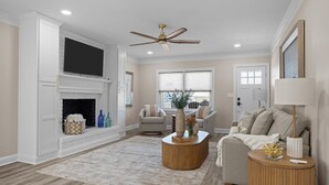 A living room with a fireplace, a ceiling fan, and a sofa. - Buddy's Sandcastle: room for family, friends, and pets. Fenced yard. (Atlantic Beach)