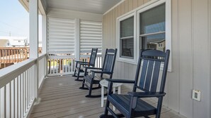A covered porch with wooden railings, a series of Adirondack chairs, and a view of the neighborhood. - Buddy's Sandcastle: room for family, friends, and pets. Fenced yard. (Atlantic Beach)