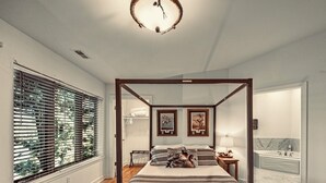 A four-poster bed with a wooden frame, a large window with blinds, and a view of a bathroom with a bathtub and a marble countertop. -  Dells treetop lakeside lodging on famous Canyon Road. A top location! (Wisconsin Dells)